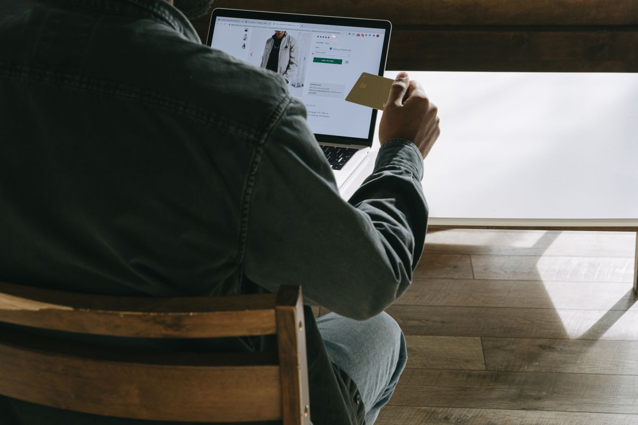 Adult man using a laptop while holding a credit card for online shopping in a comfortable indoor setting.